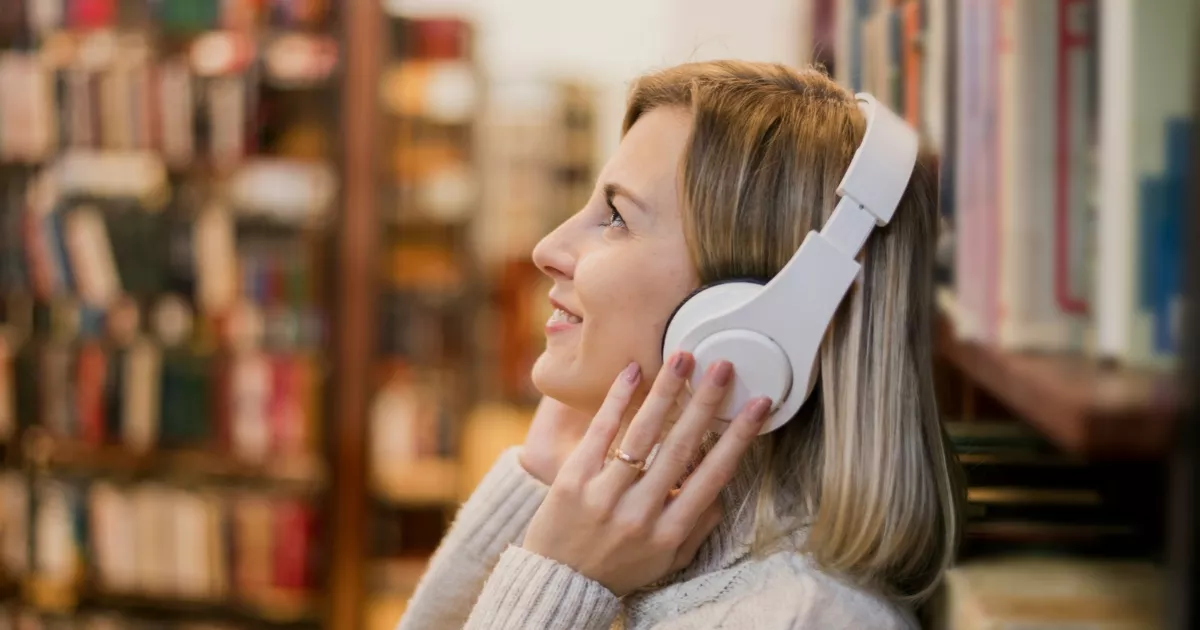 Mulher usando fones de ouvido diante de estantes de livros em uma livraria.