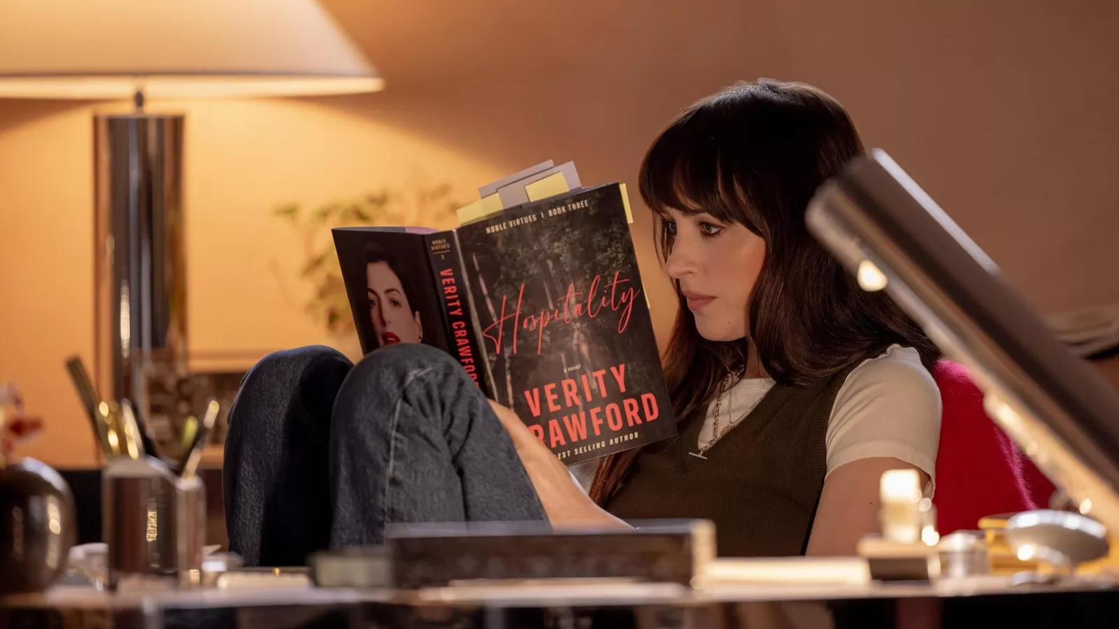 Dakota Johnson como Lowen Ashleigh lê um romance de Verity Crawford com a foto de Anne Hathaway na orelha, em cena do filme Verity, adaptação do suspense de Colleen Hoover