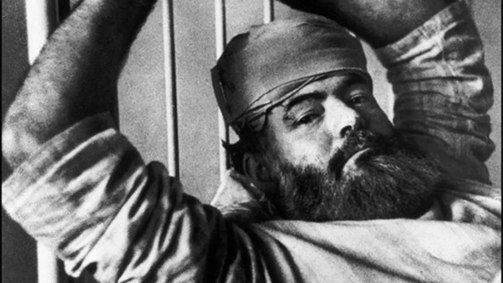 Retrato em preto e branco de Ernest Hemingway mais velho, de barba e usando uma bandana na cabeça.