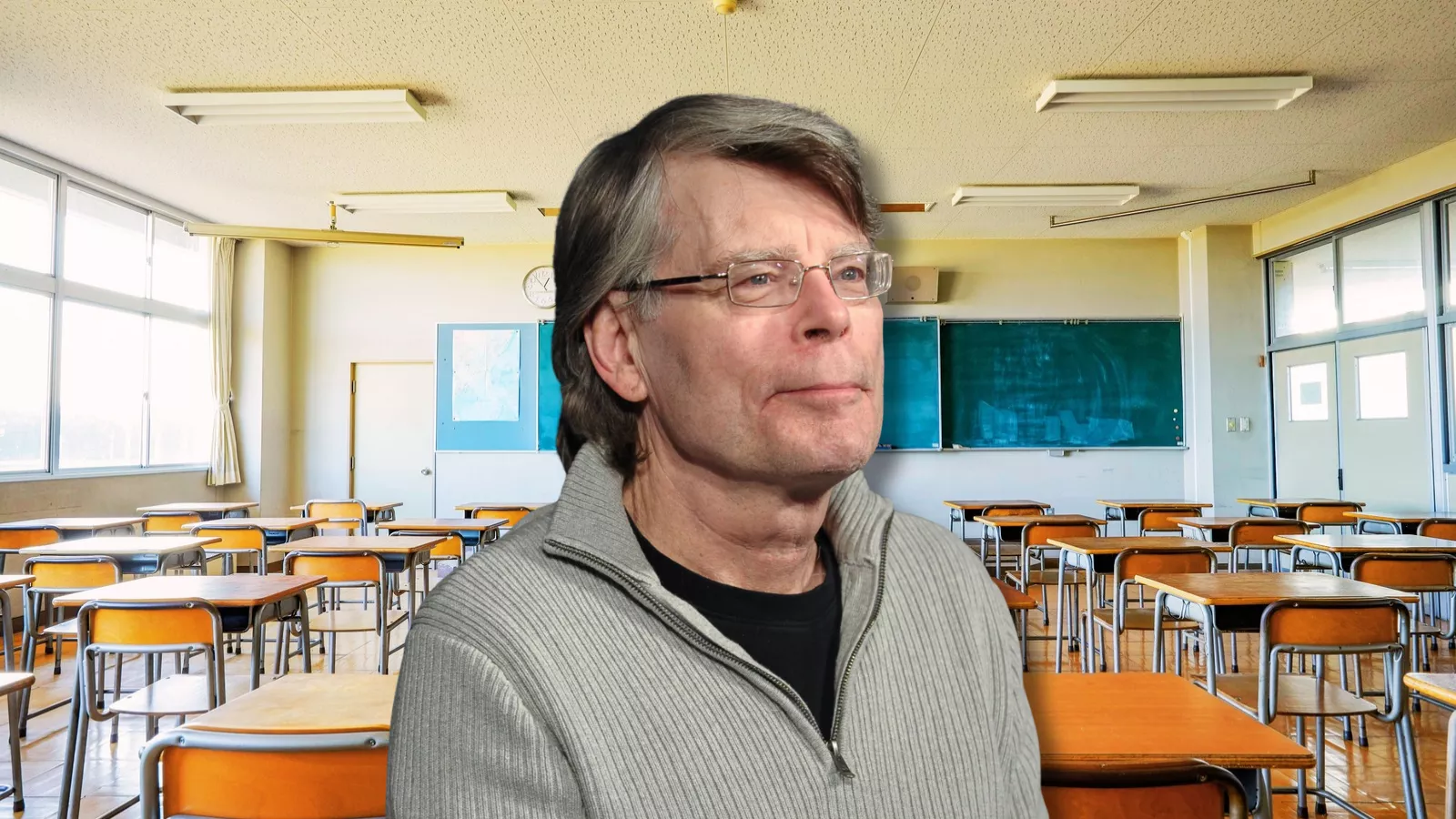 Stephen King em primeiro plano diante de uma sala de aula escolar vazia, com carteiras e quadro-negro ao fundo.