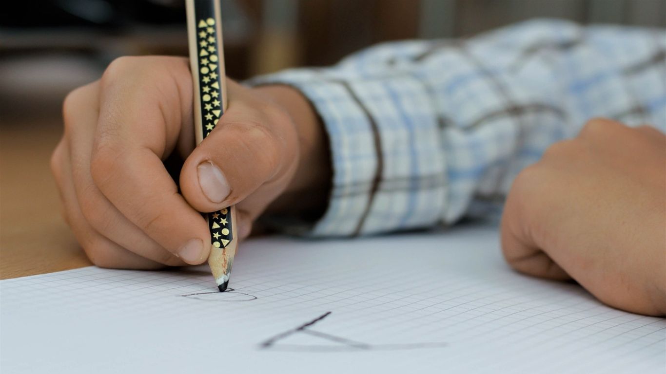 Criança escrevendo em um papel com um lápis - imagem para uma postagem sobre um plano de aula a respeito de Poesia Visual