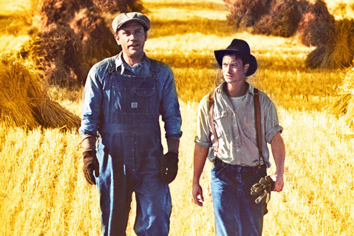 A capa do filme Ratos e Homens, mostrando dois homens, em roupas tradicionais do campo, andando em uma plantação de trigo