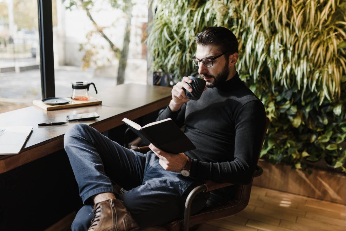 Um estudante de letras sentado, tomando café e lendo um livro