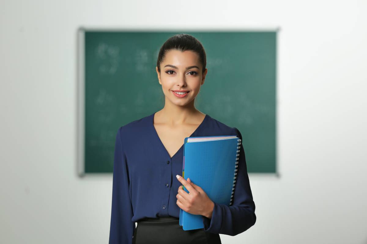 Uma estudante de Letras, segurando seus cadernos, com um fundo com um quadro de escola