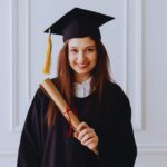 Jovem mulher com roupa de formatura segurando o diploma