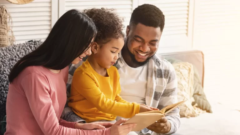 Família reunida em um momento de leitura e carinho: pai, mãe e filha pequena sentados juntos no sofá, sorrindo e lendo um livro infantil. A cena transmite afeto, conexão e celebração da presença paterna, ideal para ilustrar conteúdos sobre Dia dos Pais, infância e vínculo familiar.