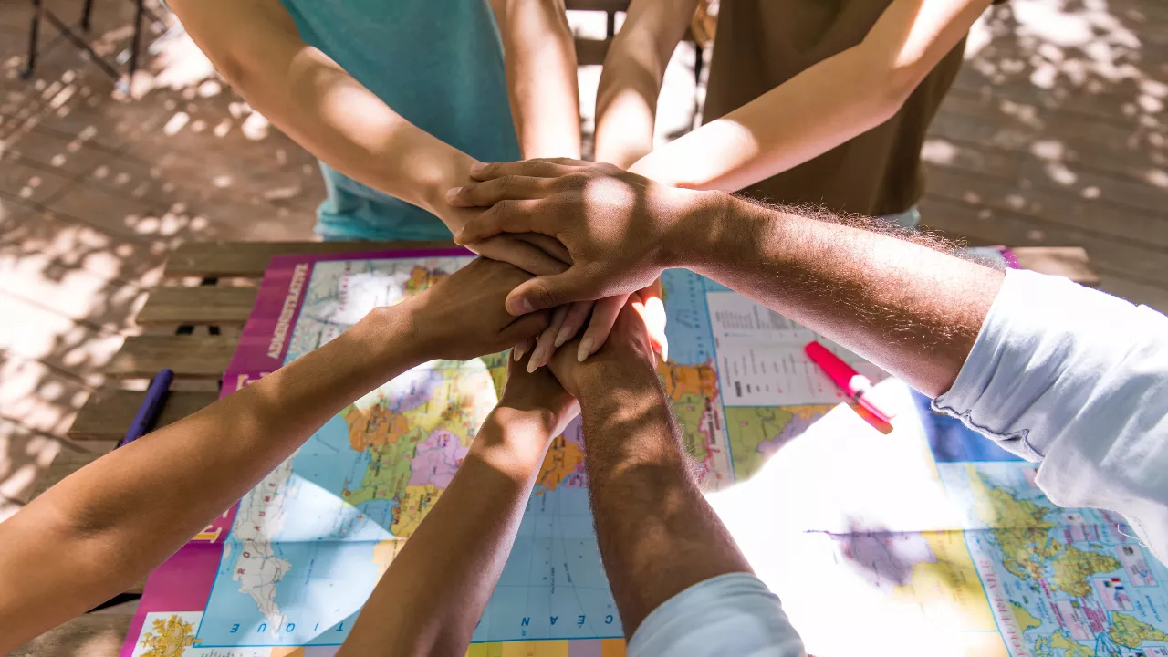 Mãos de pessoas de diferentes tons de pele unidas sobre um mapa-múndi, simbolizando diversidade, união e colaboração. A imagem representa o trabalho coletivo e o respeito às diferenças culturais, valores centrais na abordagem da Consciência Negra na Educação Infantil.
