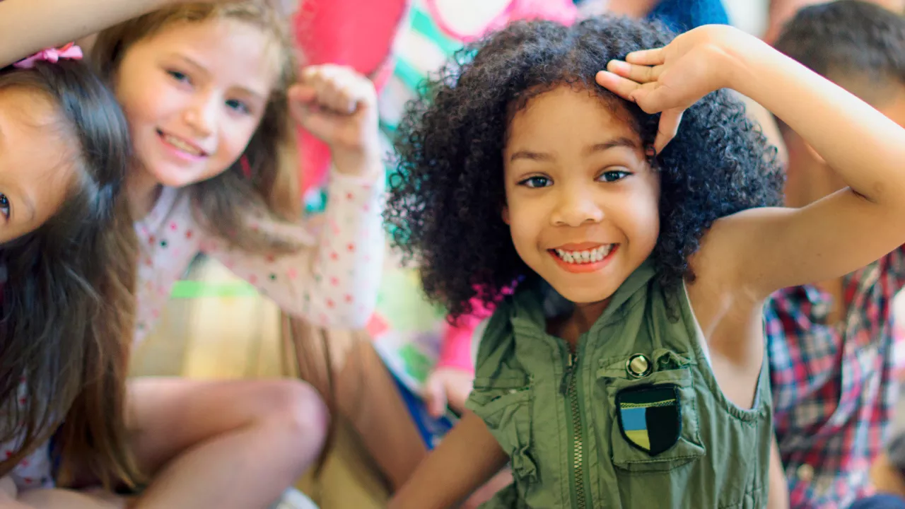 Crianças sorridentes brincam juntas, com destaque para uma menina negra de cabelo crespo em primeiro plano, expressando alegria e autoconfiança. A imagem reflete o impacto positivo de práticas pedagógicas que valorizam a identidade e fortalecem a autoestima desde a Educação Infantil.